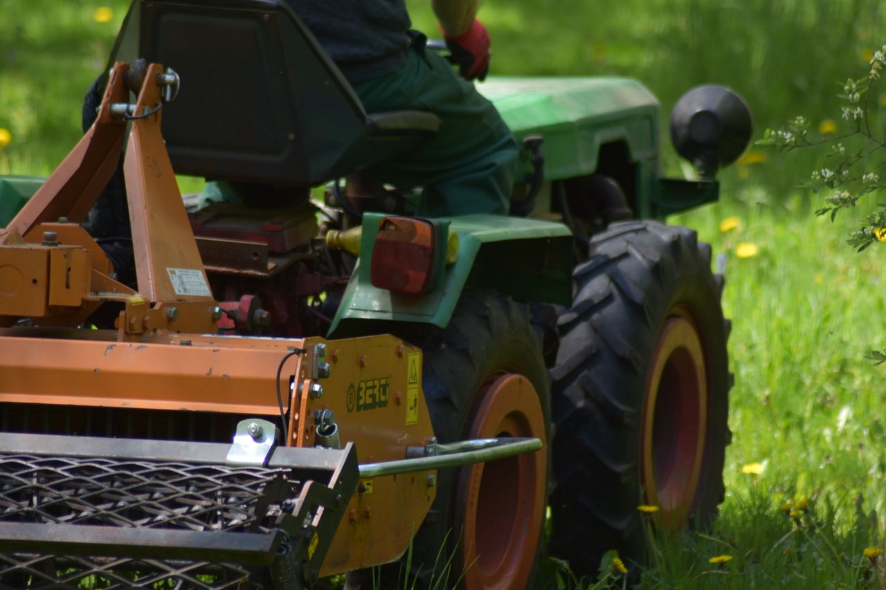 services-01 Rear view of a man using a tractor mower in a lush green field during summer.