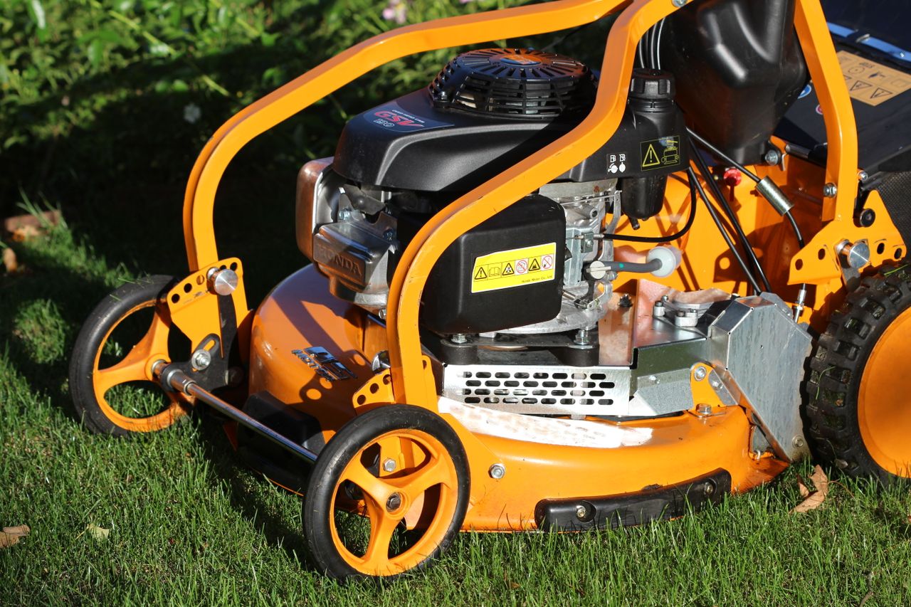 services-02 Vibrant orange lawn mower standing on fresh green grass, capturing outdoor maintenance theme.