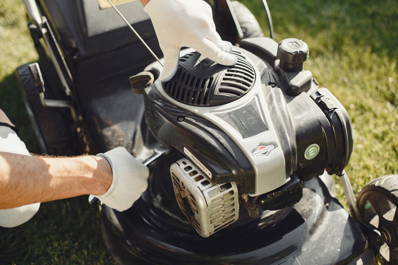 who-we-are Hands in gloves adjusting a lawn mower outdoors, perfect for gardening themes.