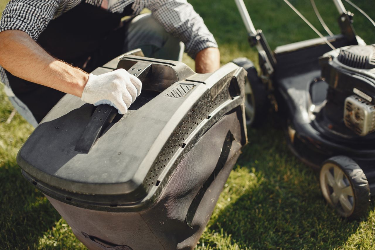 team-03 An adult man replacing a lawn mower bag on a sunny day in the yard.