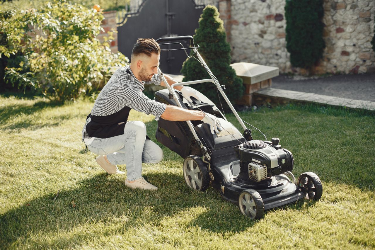 team-04 Man in summer attire using a lawnmower on a sunny day, showcasing gardening tools.