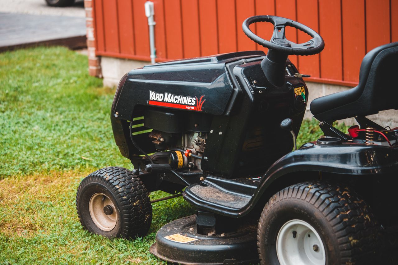 Mastering the First Impression: Your intriguing post title goes here Close-up of a black riding lawn mower parked on a lawn next to a red building.